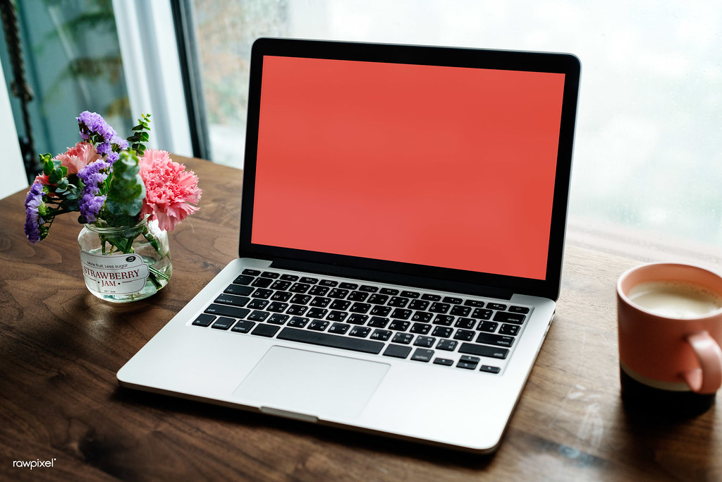 Laptop with a red screen beside flowers and a coffee mug on a wooden table