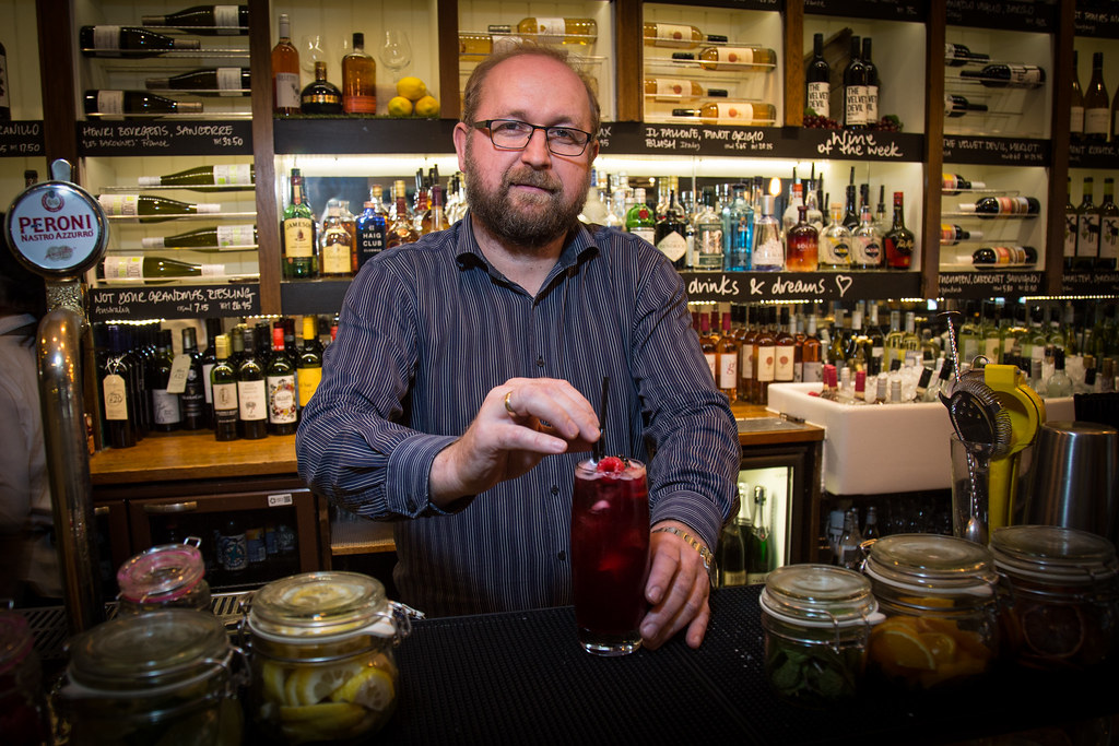 Bartender garnishing a red drink in front of shelves stocked with wine and spirits
